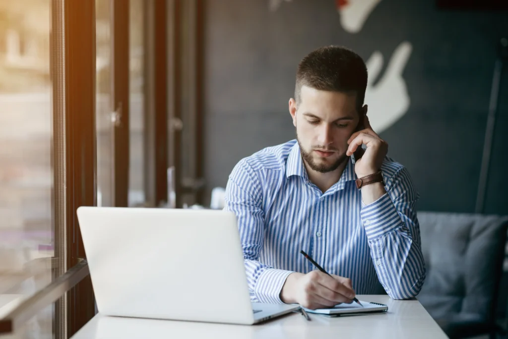 Man achter een laptop die aan het bellen en aan het schrijven is