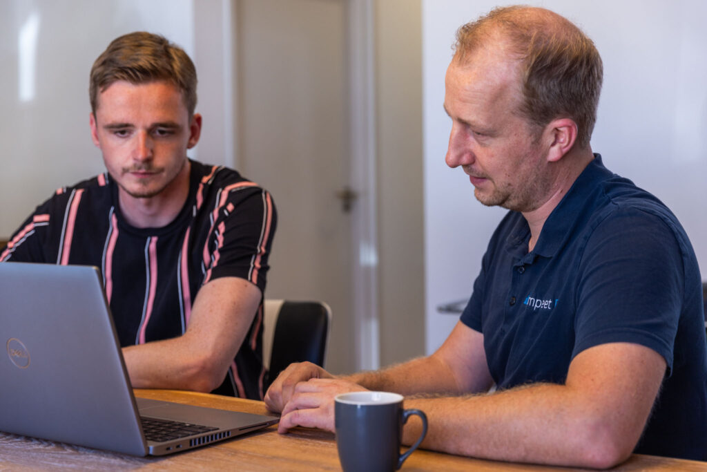 Digitale veiligheid: Twee mannen die aan het praten zijn. Een man geef uitleg aan de andere man en beide kijken ze naar de laptop.