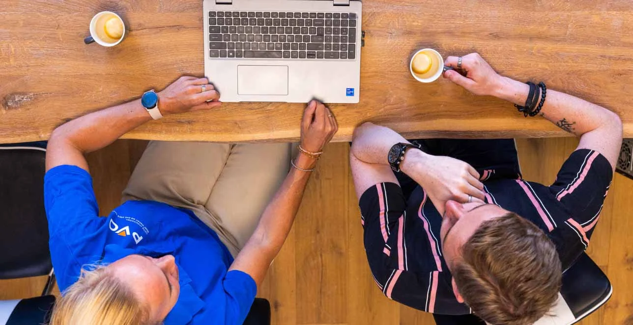 Foto van bovenaf gemaakt waar een laptop op tafel staat en twee mensen naar het scherm kijken